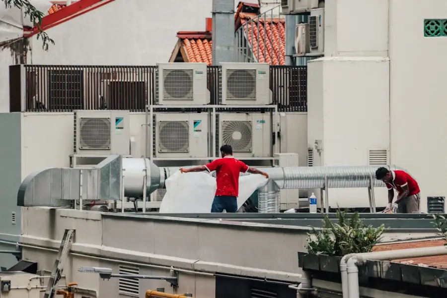 Dois técnicos trabalhando entre condensadoras de ar-condicionado num telhado